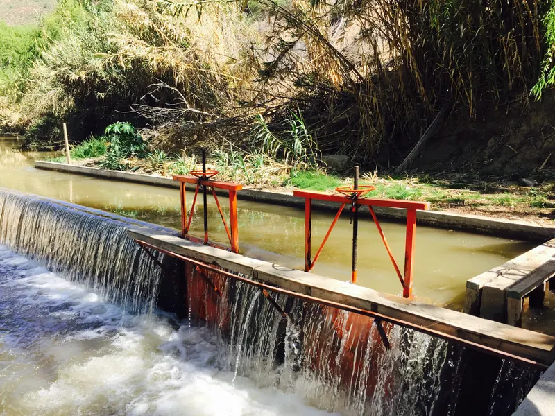 Compuertas metálicas de color naranjo sobre un canal de agua turbia, entre cañaverales